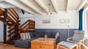 A room with a wooden staircase, a gray sofa, a wooden coffee table, and a gray armchair. - Holiday house North Sea Mermaid (Esens)