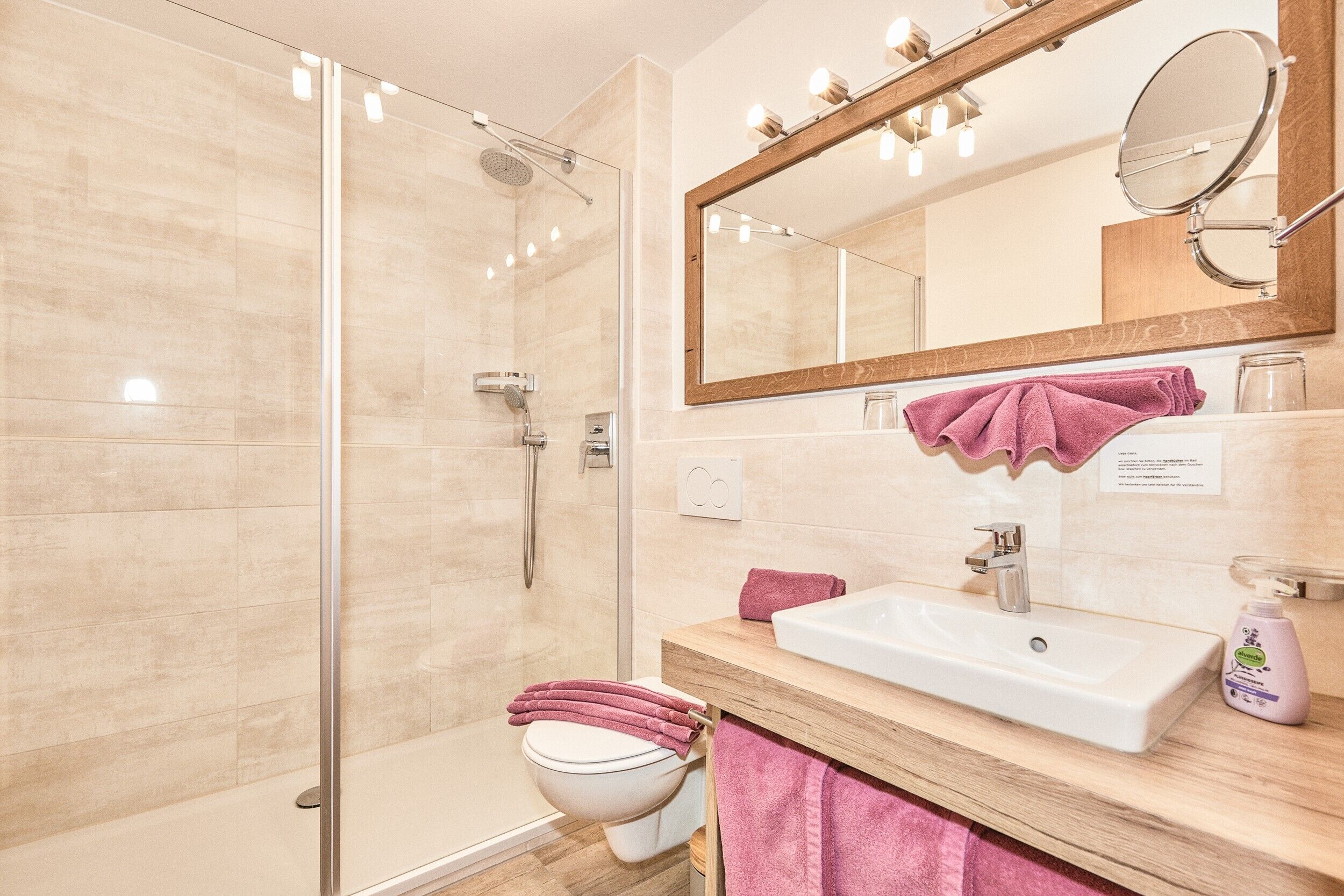 A modern bathroom with a glass shower enclosure, a white sink, and a large mirror with lights.