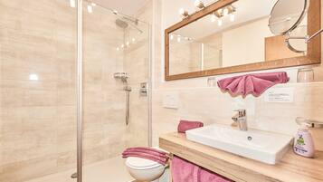 A modern bathroom with a glass shower enclosure, a white sink, and a large mirror with lights.