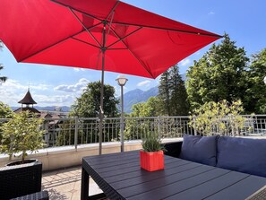 Een terras met een rode parasol, een tafel en een plant in pot.