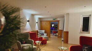 A modern living room with a wooden floor, red and grey sofas, a glass coffee table, and a wooden door leading to a dining area.