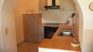A compact kitchen with a built-in dishwasher, a sink, and a stove. - Two-room vacation apartment 60sqm, shower/WC, extra bedroom, kitchen, terrace (Reit im Winkl)