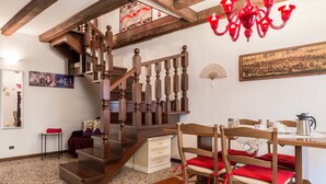 Una escalera de madera con un candelabro, una mesa de comedor con sillas y un ventilador en la pared.