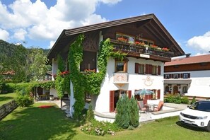 Un chalet traditionnel doté d’un balcon orné de fleurs, d’un jardin bien entretenu et d’une voiture garée devant.