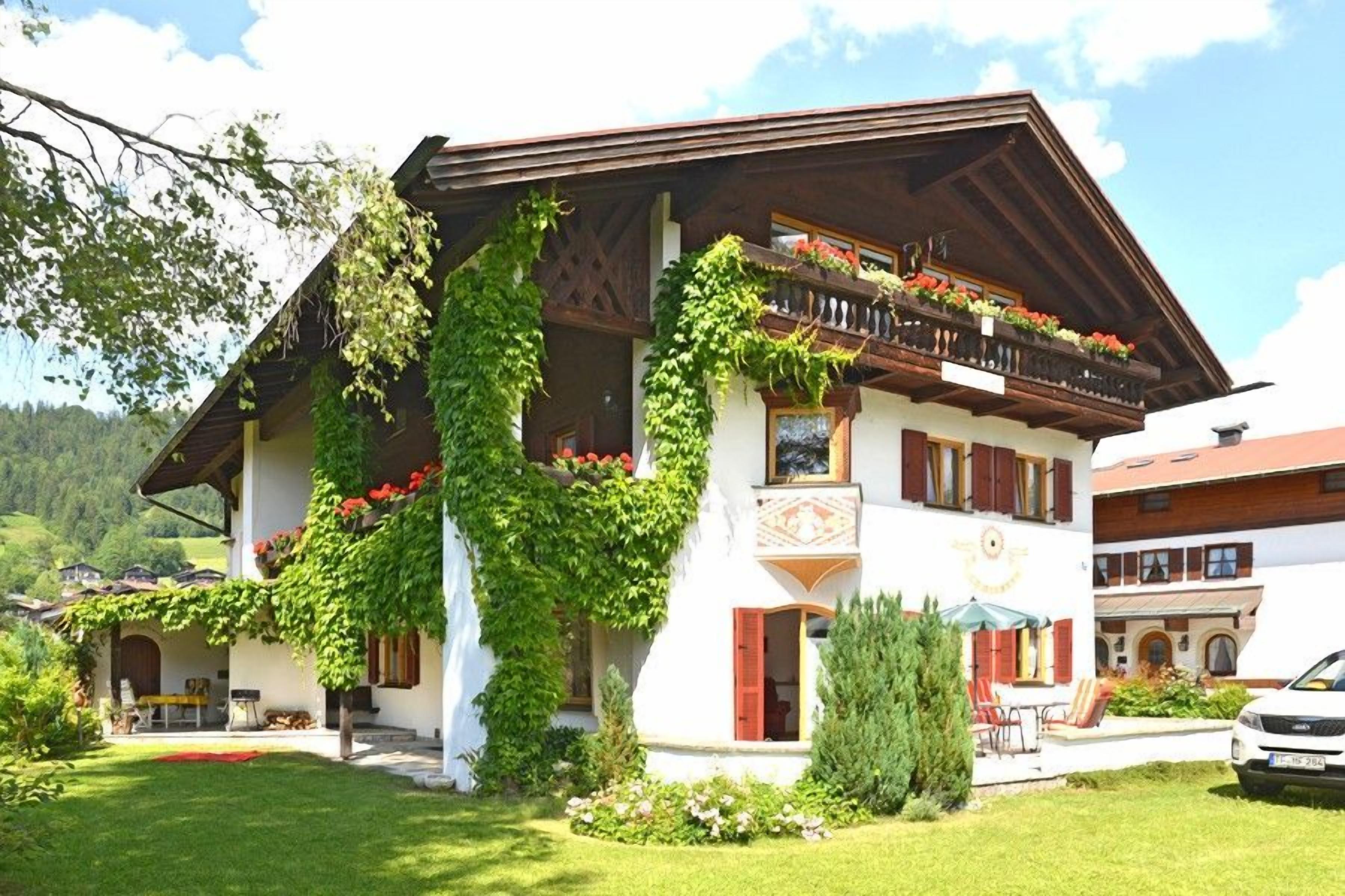 A traditional chalet with a balcony, a covered outdoor seating area, and a well-maintained garden.