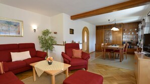 Un salon avec des canapés rouges, une table basse en bois et un coin repas comprenant une table et des chaises en bois.