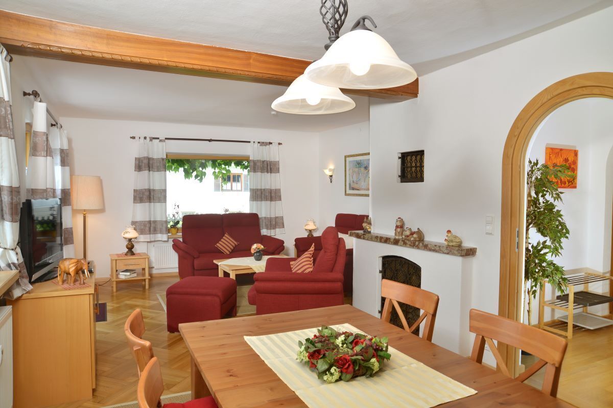 A cozy living room with a red sofa set, a wooden dining table with a floral centerpiece, and a fireplace.