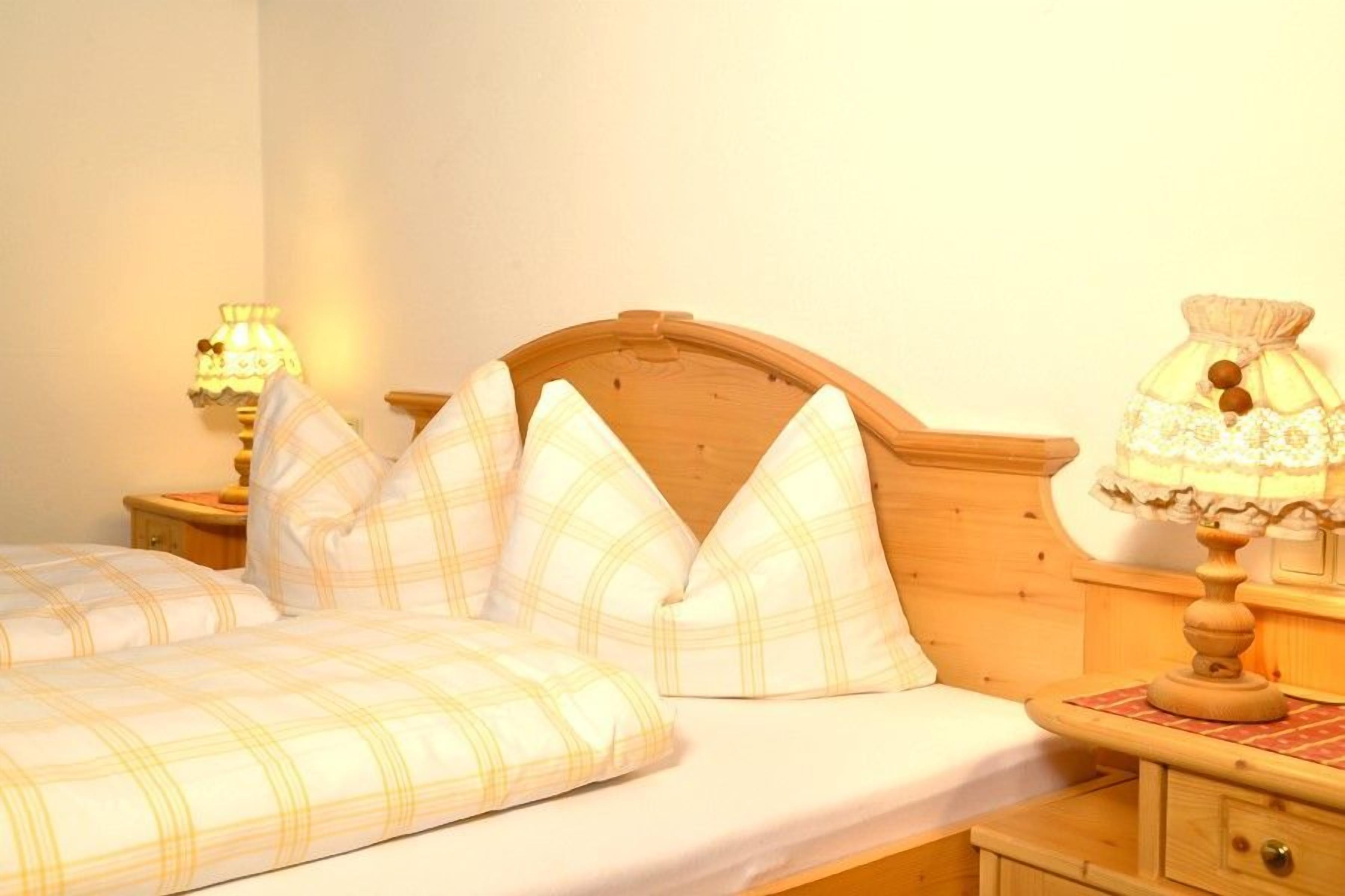 Uma cama com cabeceira de madeira, duas mesas de cabeceira com abajures e uma mesa de apoio com um abajur.