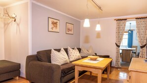 A cozy living room with a brown sofa, a wooden table, and a dining area with a chair.