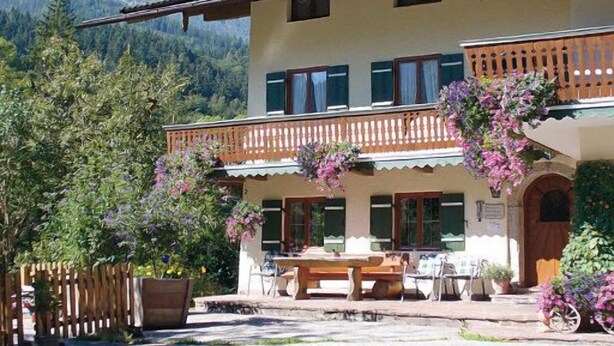 A two-story building with a balcony, outdoor seating, and a mountain backdrop.