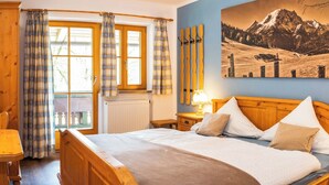 A bedroom with a wooden bed, a window with curtains, a radiator, and a mountain landscape painting on the wall.
