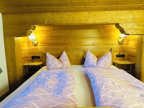 Une chambre de style cabane en bois, avec deux lits, une table de chevet et des lampes fixées au mur.