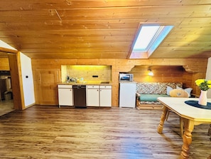 A wooden interior with a kitchen, a dining area, and a loft bedroom with a skylight.