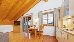 A cozy kitchen with wooden cabinets, a dining table, and a view of the mountains through the windows. - (4) Giebelstüberl -1-Zimmer Appartement , ca. 30qm, 1-2 Personen, Wohn/Schlafraum, Kochnische, Balkon (Reit im Winkl)