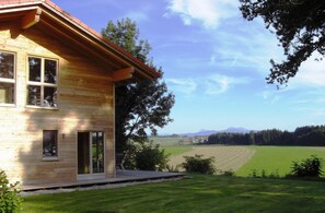 Una casa de madera con amplios ventanales y vistas a un campo verde y montañas.