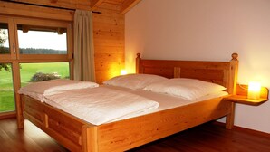 A wooden bed with two pillows and a bedside table with a lamp, in a room with wooden walls and a large window. - House Efeu 90m², up to 6 persons, 3 separate bedrooms (Traunwalchen)