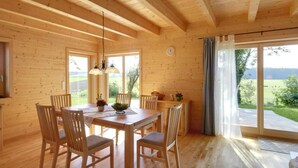 A wooden interior with a dining area, large windows, and a view of the outdoors. - House Efeu 90m², up to 6 persons, 3 separate bedrooms (Traunwalchen)