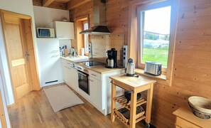 A compact kitchen with wooden walls, a microwave, a stove, a sink, and a window with a view of the outdoors. - House Efeu 90m², up to 6 persons, 3 separate bedrooms (Traunwalchen)