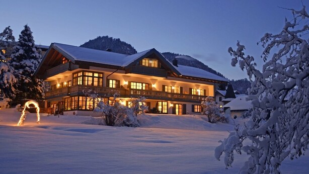 A large, multi-story lodge with a snow-covered landscape and mountains in the background. - Apartment 4, 37sqm Kienberg, balcony, kitchenette, 1 bedroom, 1 bedsit. (Ruhpolding)