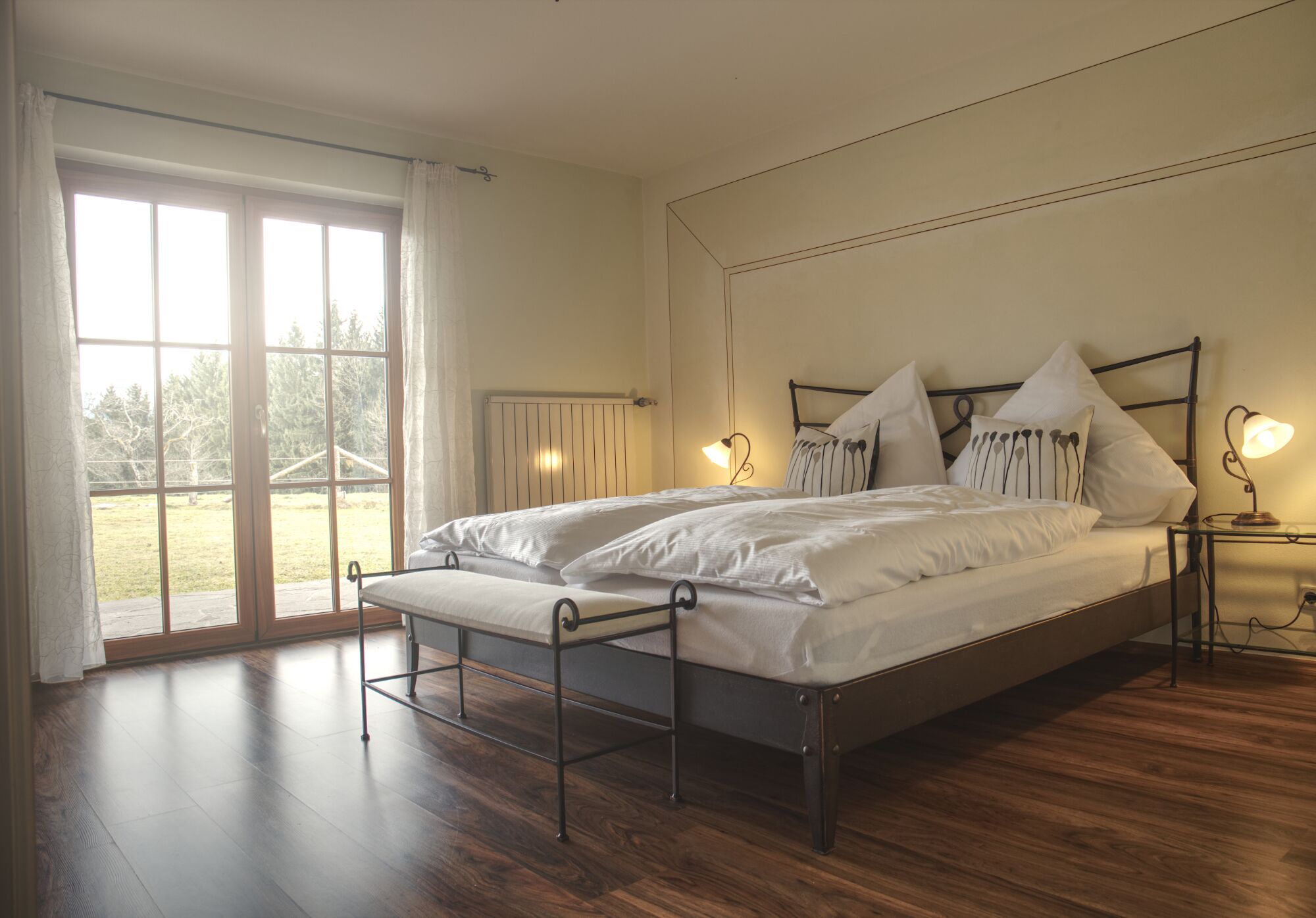 Ein Schlafzimmer mit Bett, Nachttischlampen und Blick durch ein großes Fenster.