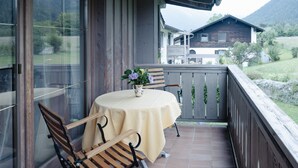 A wooden deck with a table and chairs, a potted plant, and a view of a mountain and house in the background. - Apartment Predigtstuhl 55 sqm for max. 3 persons, 1 bedroom, mountain view (Bayerisch Gmain)