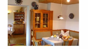 A dining area with a wooden cabinet, a table set for two, and a clock on the wall. - Apartment Predigtstuhl 55 sqm for max. 3 persons, 1 bedroom, mountain view (Bayerisch Gmain)