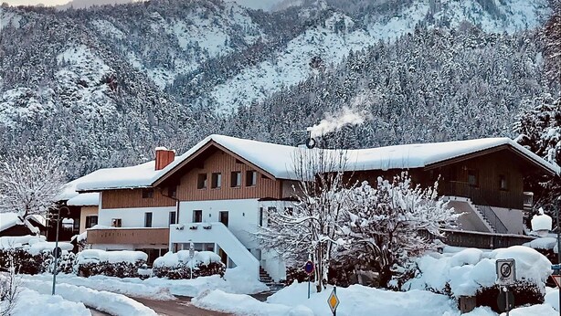 A wooden chalet-style building with a snow-covered roof, surrounded by a snowy landscape and mountains in the background. - Apartment Predigtstuhl 55 sqm for max. 3 persons, 1 bedroom, mountain view (Bayerisch Gmain)