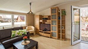 En moderne stue med sofa, sofabord, fjernsyn, træhylder og en skydedør til haven.