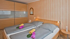 Et hotelværelse med to senge, trægavle, et lille bord med lampe og et dekorativt spejl på væggen.