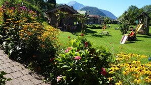 A garden with a wooden playhouse, a picnic table, and a slide. - Ferienwohnung Kneifelspitze für 2-6 Personen, 88 qm (Marktschellenberg)