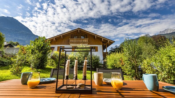 A wooden deck with a table set for breakfast, surrounded by lush greenery and mountains in the background.