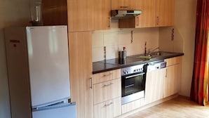 A compact kitchen with wooden cabinets, a built-in oven, and a refrigerator. - Apartment Baumgart for max. 3 persons, 35 sqm, 1 bedroom, balcony (Schönau am Königssee)