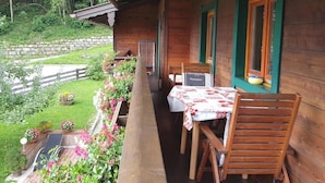 A wooden cabin with a balcony, a table with chairs, and a stone wall in the background. - Apartment Baumgart for max. 3 persons, 35 sqm, 1 bedroom, balcony (Schönau am Königssee)