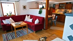 Een gezellige woonkamer met een rode bank, een houten salontafel en een zichtbare keuken door een open doorgang.
