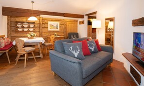 A cozy living room with a grey sofa, wooden dining table, and a TV on a stand. - Ferienwohnung (6) (Reit im Winkl)