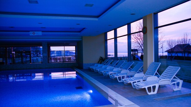 Indendørs swimmingpool med liggestole og store vinduer med udsigt over et sneklædt landskab.