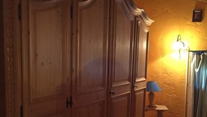 A wooden wardrobe with a curved top, a small table with a lamp, and a striped rug on a wooden floor.