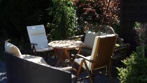 A patio area with wicker furniture, including a round table and chairs, surrounded by gravel.