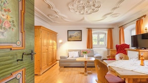 Een kamer met houten vloer, een bank, een tafel met stoelen, een televisie en een raam met gordijnen.