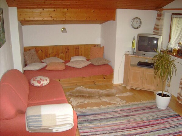 Una sala de estar acogedora con un sofá rojo, una cama pequeña con almohadas, un televisor, un reloj y una planta en maceta.