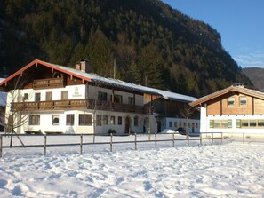Un edificio de estilo chalé tradicional con fachada de madera y techo inclinado, rodeado de un paisaje nevado y montañas boscosas.