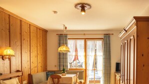 Una habitación con piso de madera, una cama con manta estampada, un sofá, una mesita de noche con lámpara y vista al exterior a través de una ventana con cortinas.