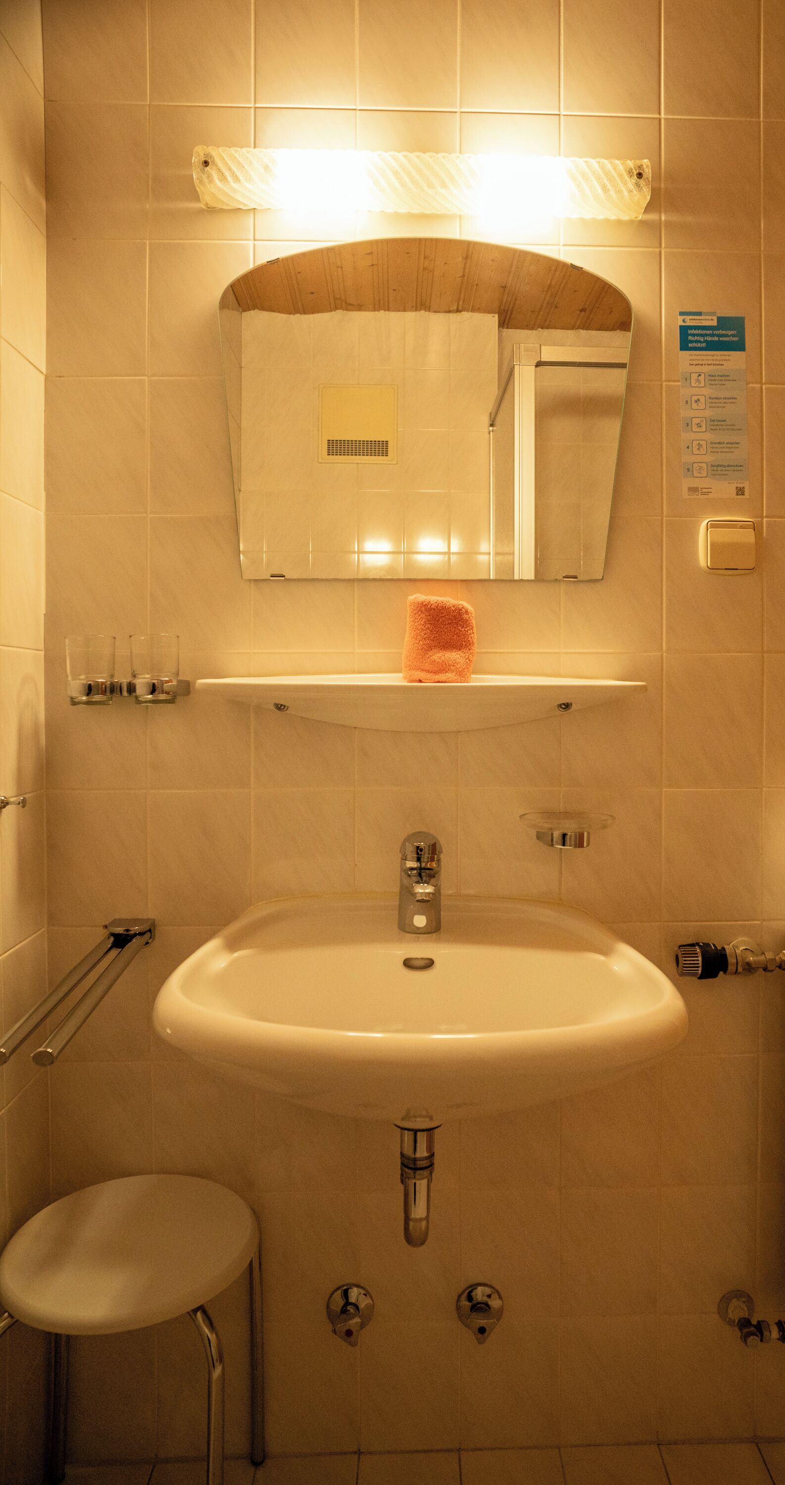 A bathroom with a sink, mirror, towel rack, and a small stool.