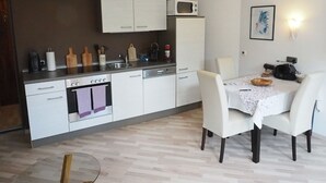 Ett kompakt kök med vita skåp, en mikrovågsugn och en matplats med ett bord och stolar.