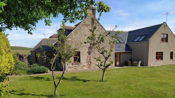 A stone house with a sloped roof, a well-maintained lawn, and a small garden area. - Chapel Of Barras Farm Bed & Breakfast (Stonehaven)