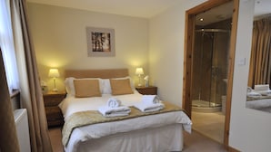 A hotel room with a large bed, two bedside tables with lamps, a shower area, and a framed picture on the wall. - Chapel Of Barras Farm Bed & Breakfast (Stonehaven)