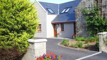 A house with a stone facade, a sloped roof, and a small garden with colorful flowers.