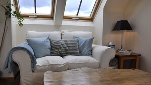 A living room with a white sofa, two pillows, a wooden coffee table, a lamp, and a plant. - Chapel Of Barras Farm Bed & Breakfast (Stonehaven)