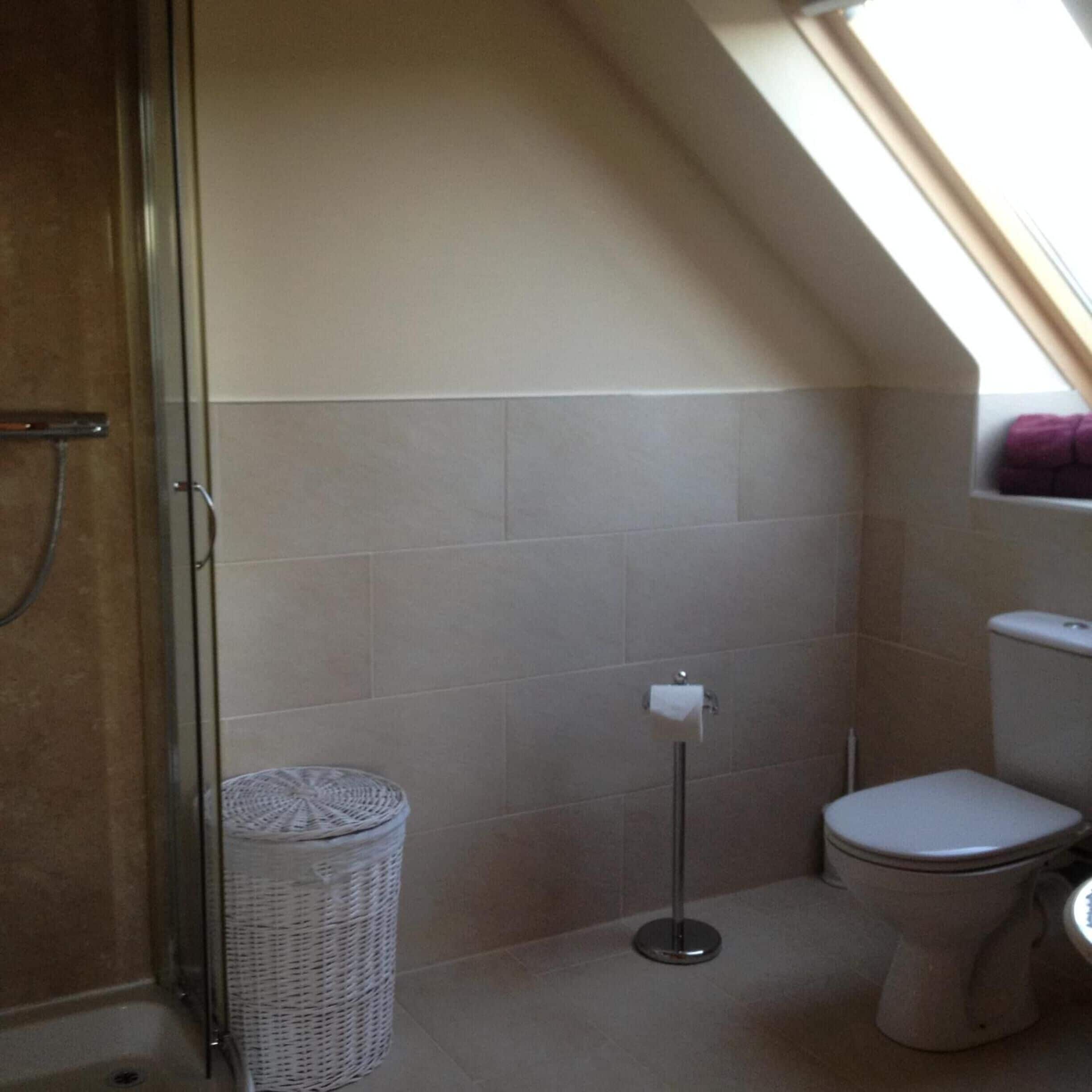 A small, single-occupancy bathroom with a shower, toilet, and a waste basket.