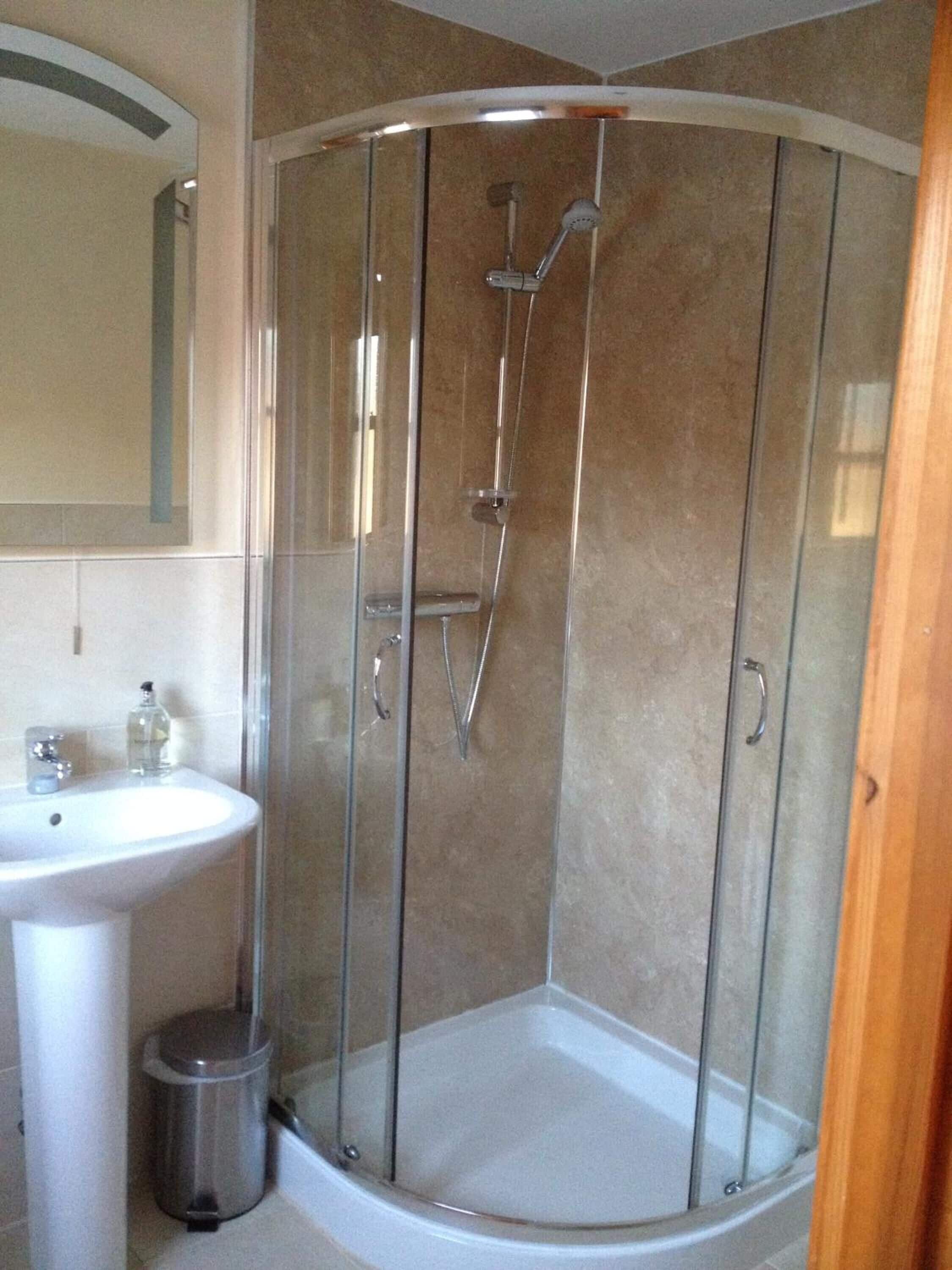 Un baño moderno con ducha de vidrio, lavamanos pedestal y un espejo.